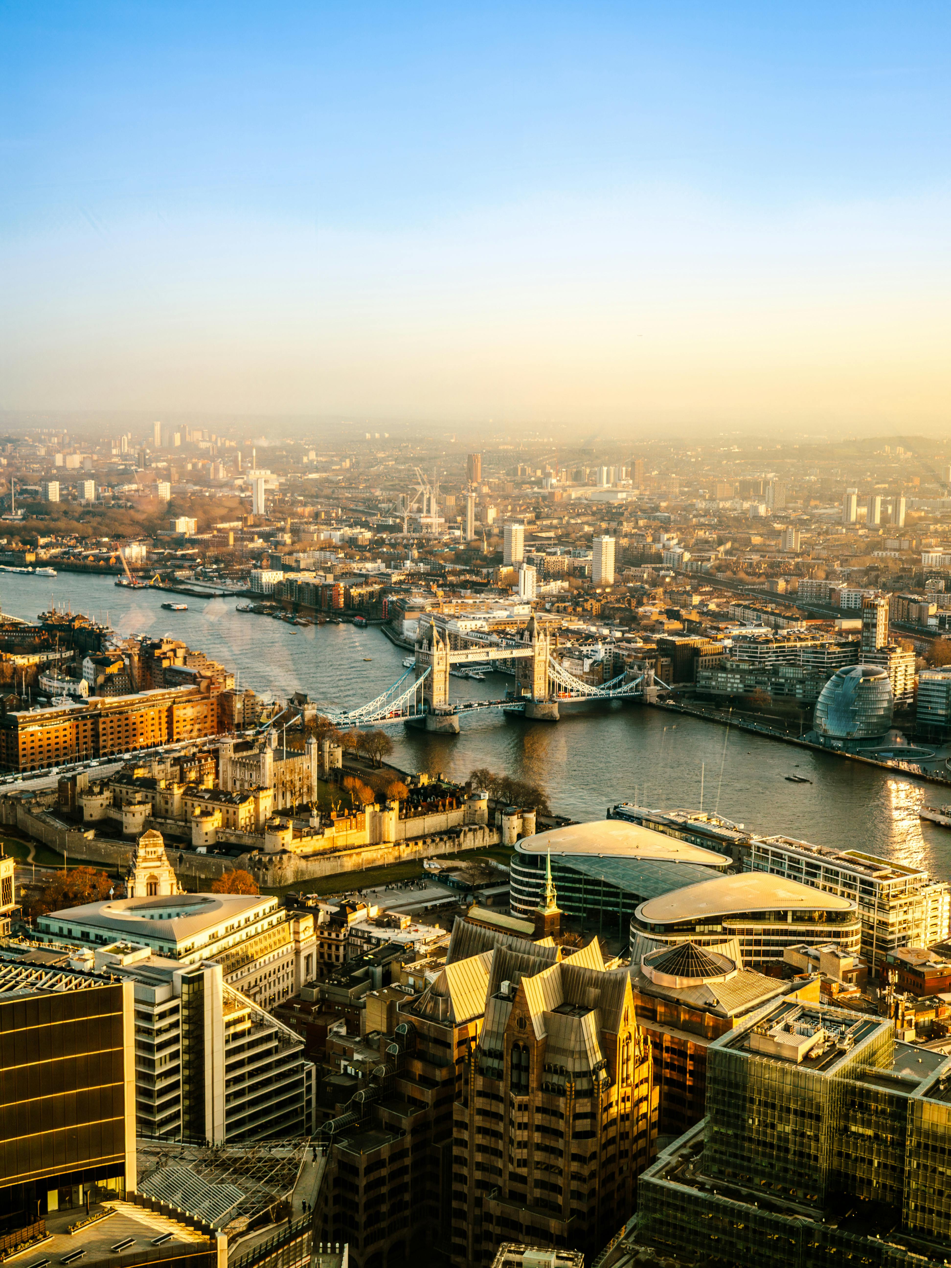 Aerial view of London with Tower Bridge over the River Thames and city buildings at sunset.
