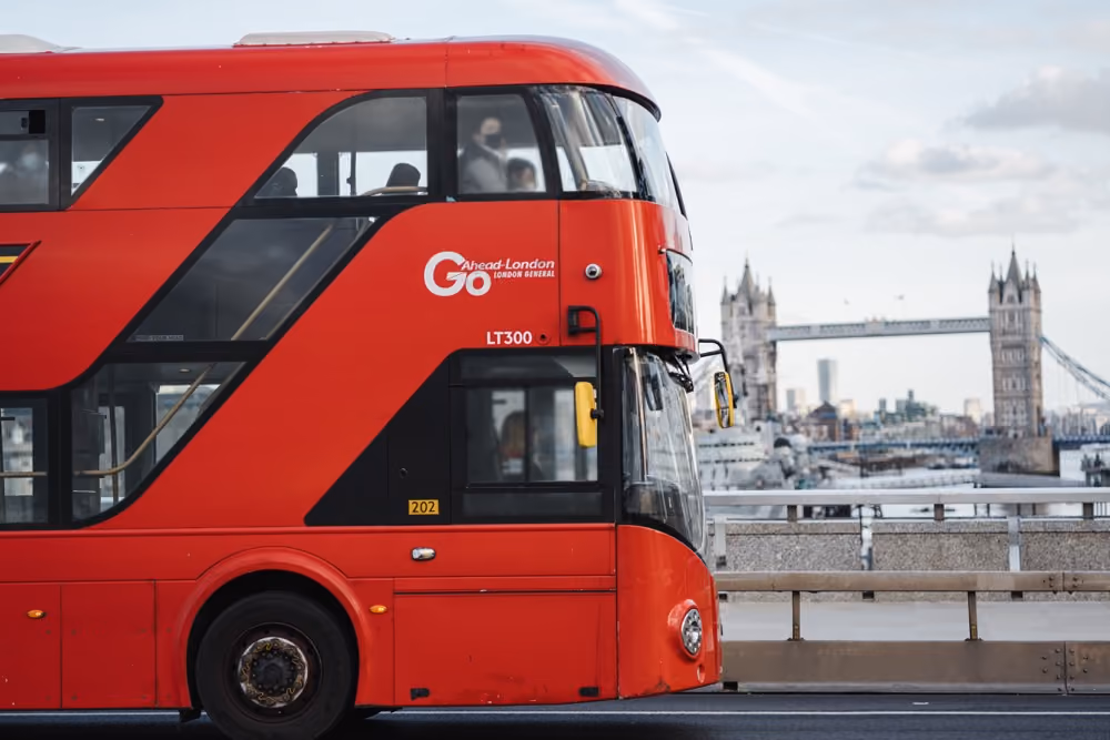 Red double-decker bus driving on a bridge with London Tower Bridge in the background.
