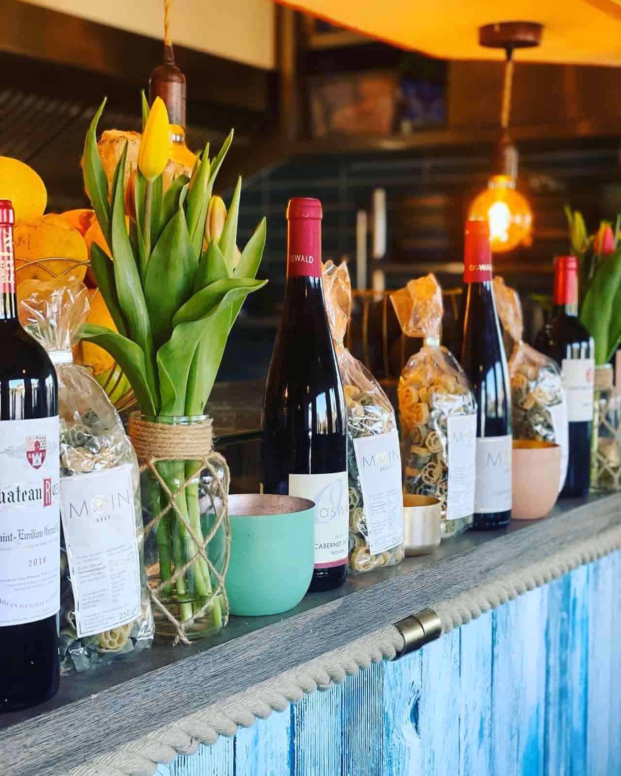 Flaschen Wein, Packungen Pasta und Vasen mit gelben Tulpen auf einer rustikalen Holztheke mit blauer Farbe.