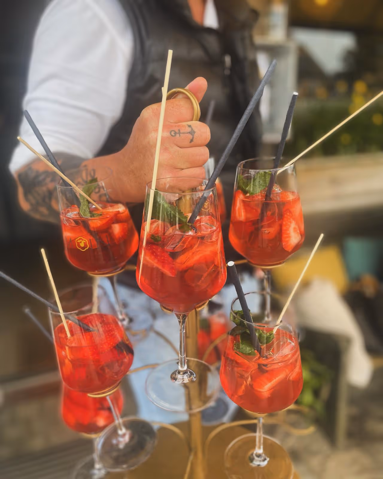 Mehrere Gläser mit rotem Erdbeer-Cocktail, Strohhalmen und Minze in einem Glasständer.