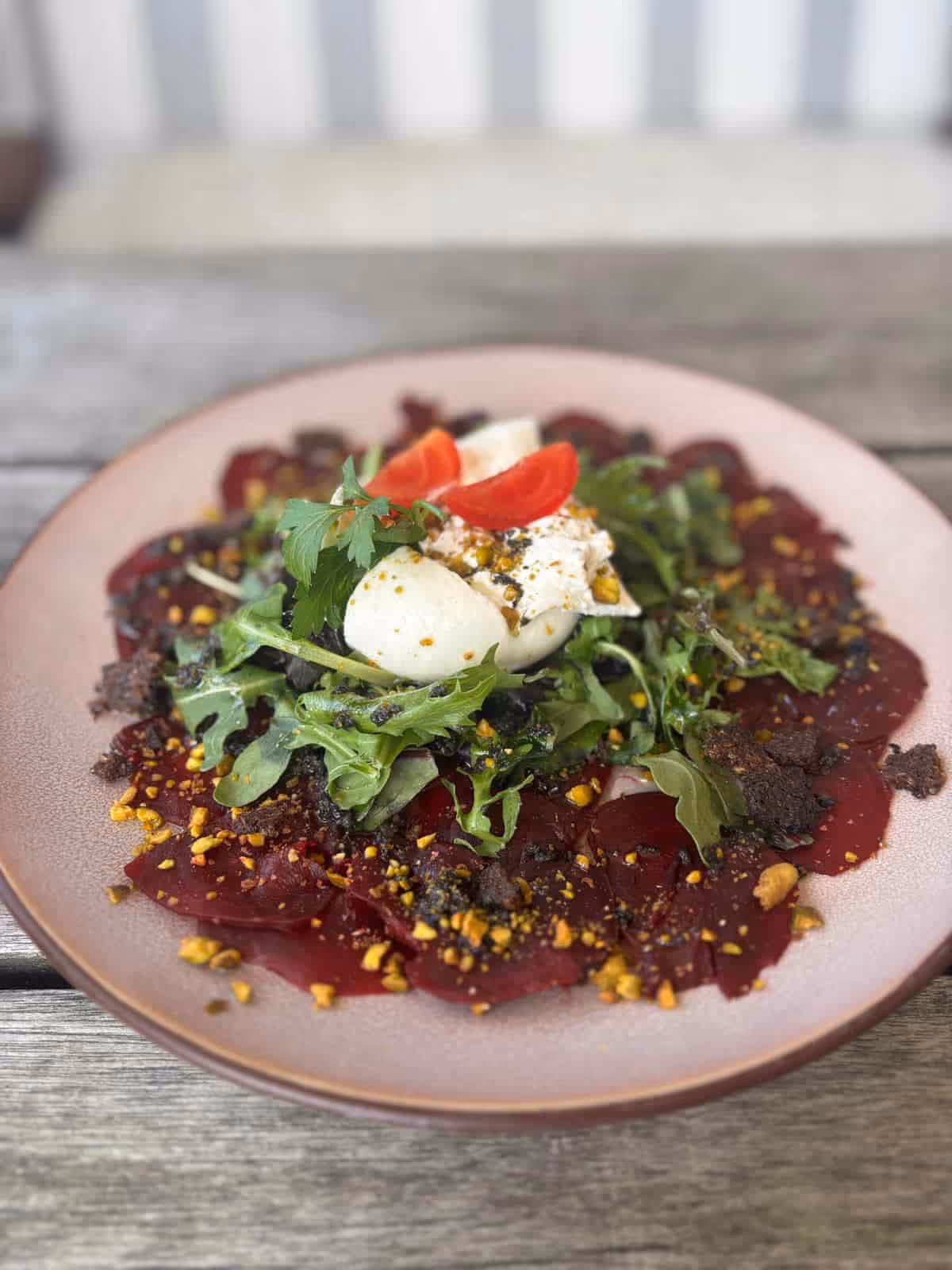 Rote Rübenscheiben mit Salat, Mozzarella, Tomaten und Gewürzen auf einem Teller.