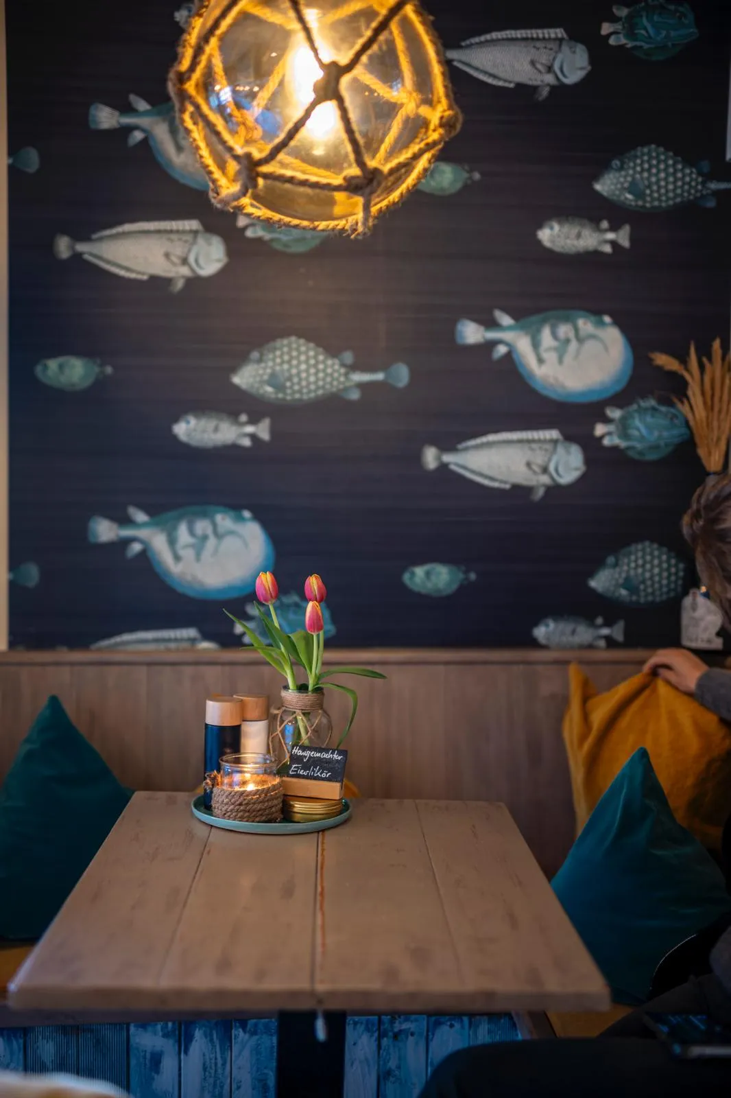 Gemütlicher Esstisch mit Tulpen, Kerze und maritim gemusterter Wand mit Fischen.