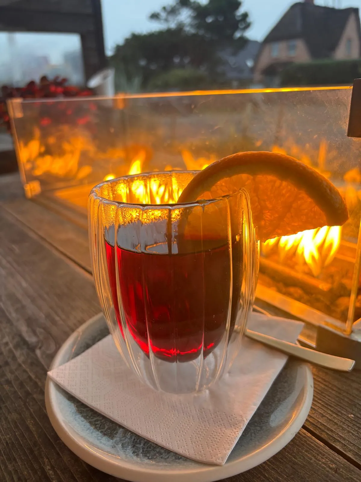 Glas mit heißem Tee und Orangenscheibe auf einem Teller vor einem Feuer im Freien.