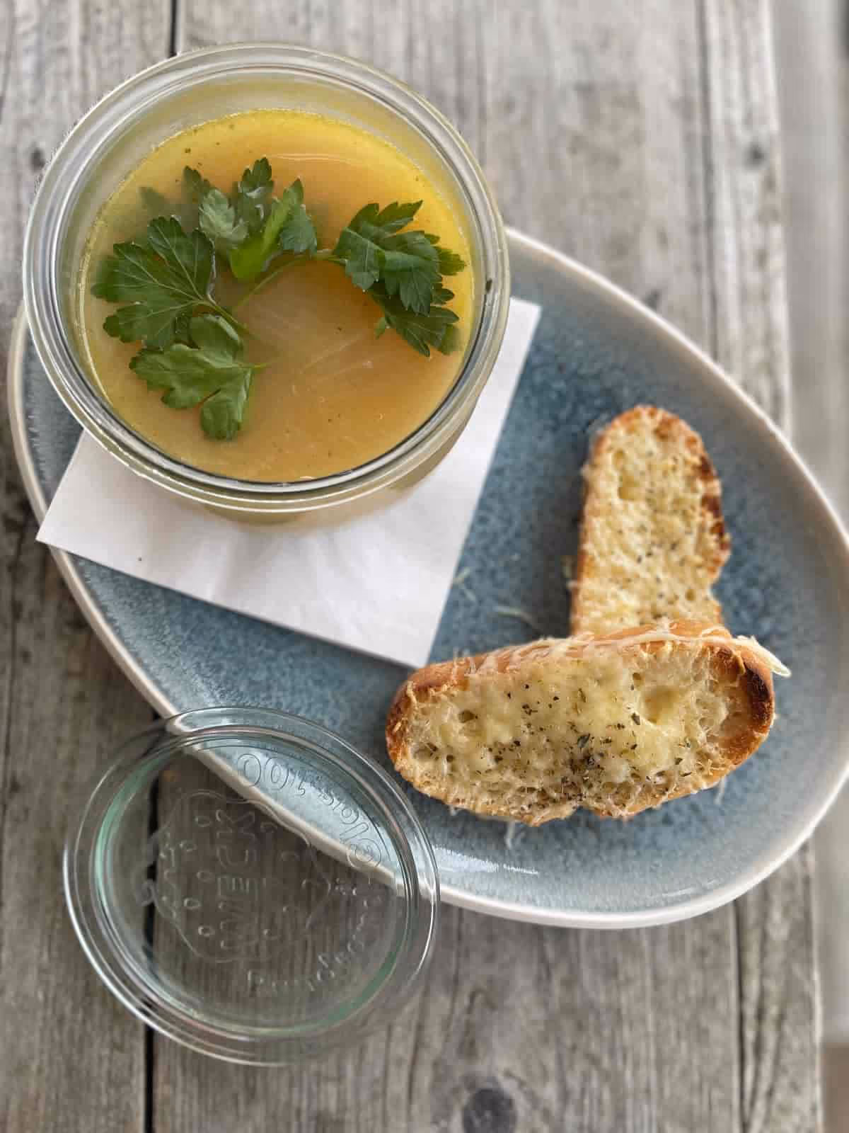 Glas mit gelber Suppe garniert mit Petersilie und zwei Scheiben geröstetem Knoblauchbrot auf blauem Teller.