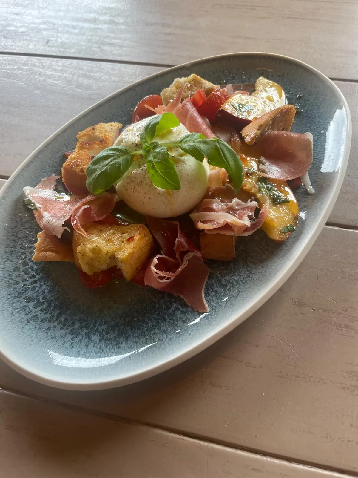 Vorspeise mit Burrata, Prosciutto, geröstetem Brot, Tomaten und Basilikum auf blauem Teller.