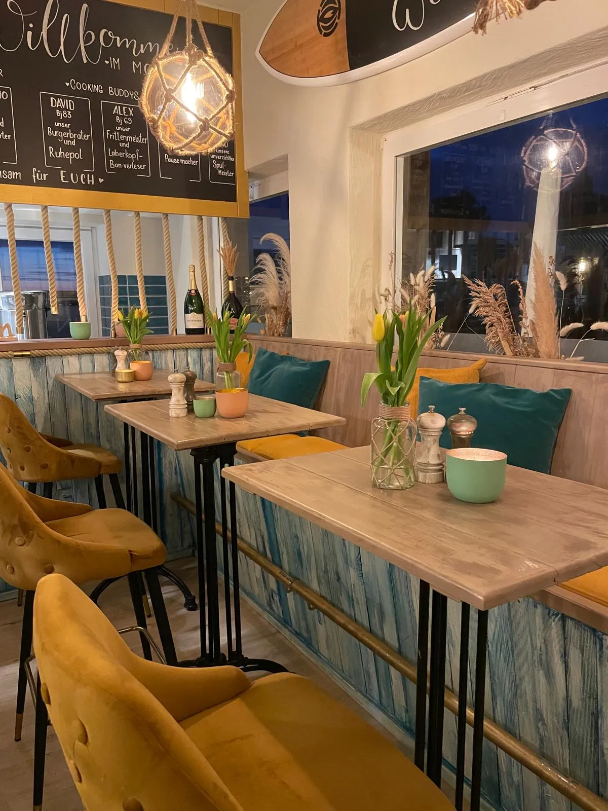 Gemütliches Café mit Holztischen, gelben Sesseln und dekorativen Blumen in Glasvasen.