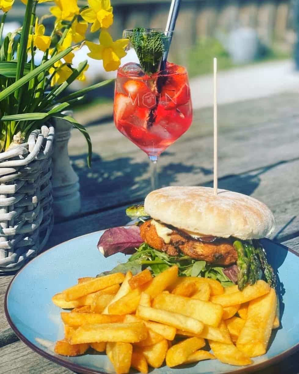 Burger mit Salat und Spargel, Pommes, daneben Glas mit rotem Getränk und Minze auf Holztisch.