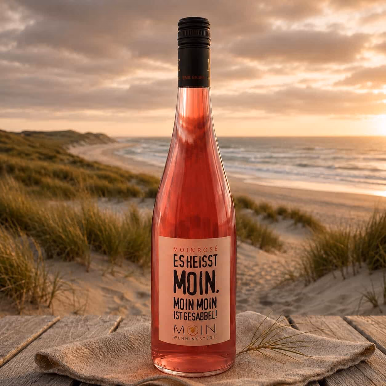 Flasche Roséwein steht auf Holzplatte mit Strand, Dünen und Sonnenuntergang im Hintergrund.