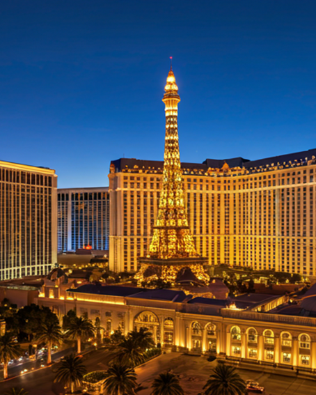 Illuminated replica of the Eiffel Tower in front of a large hotel building at dusk.