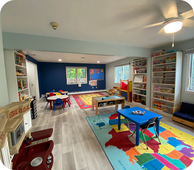 Children's playroom area with a toy kitchen set, blue baby seat, and a tall shelf filled with organized colorful toys and educational blocks next to foam climbing blocks.