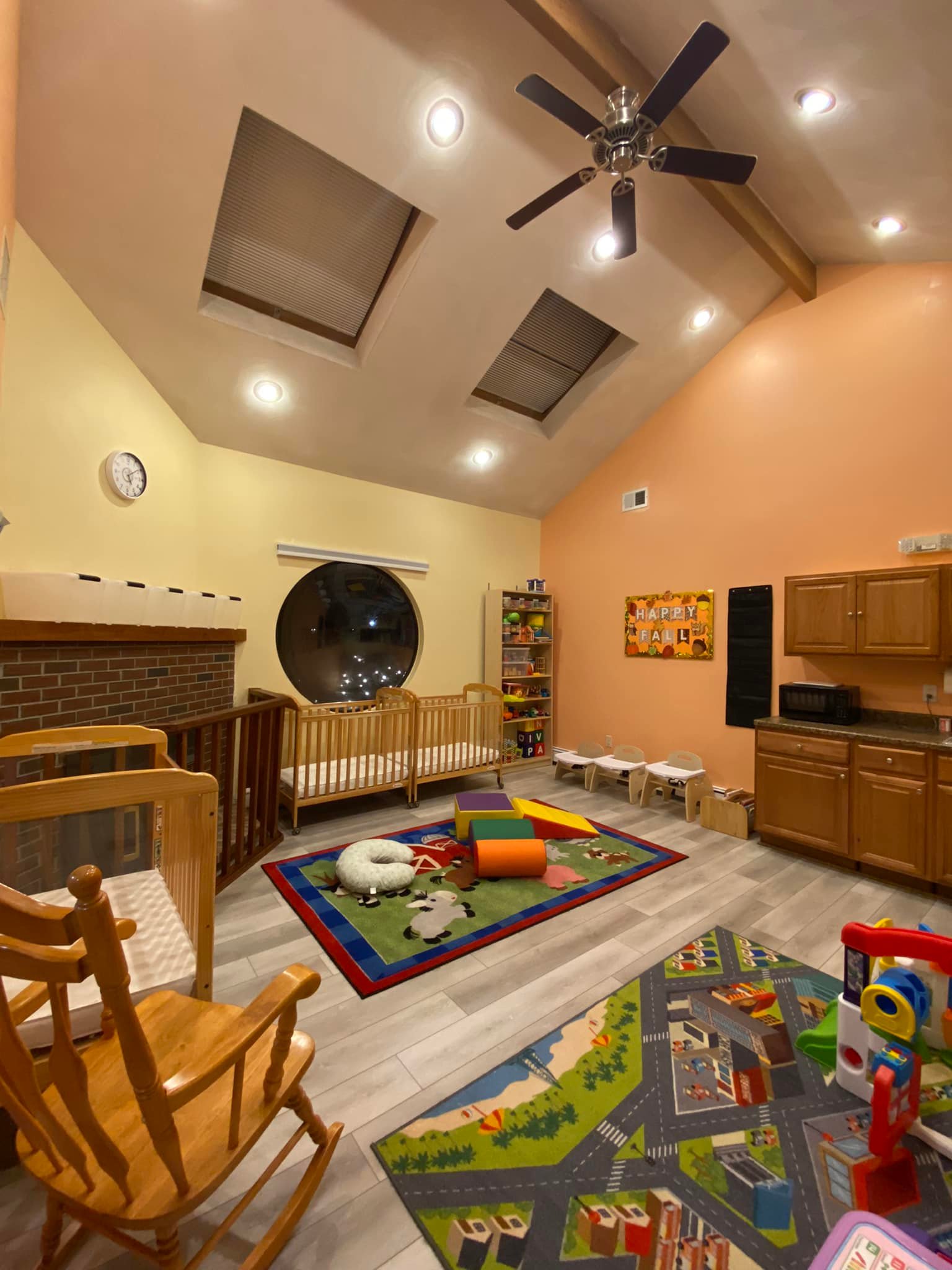 Children's playroom area with a toy kitchen set, blue baby seat, and a tall shelf filled with organized colorful toys and educational blocks next to foam climbing blocks.