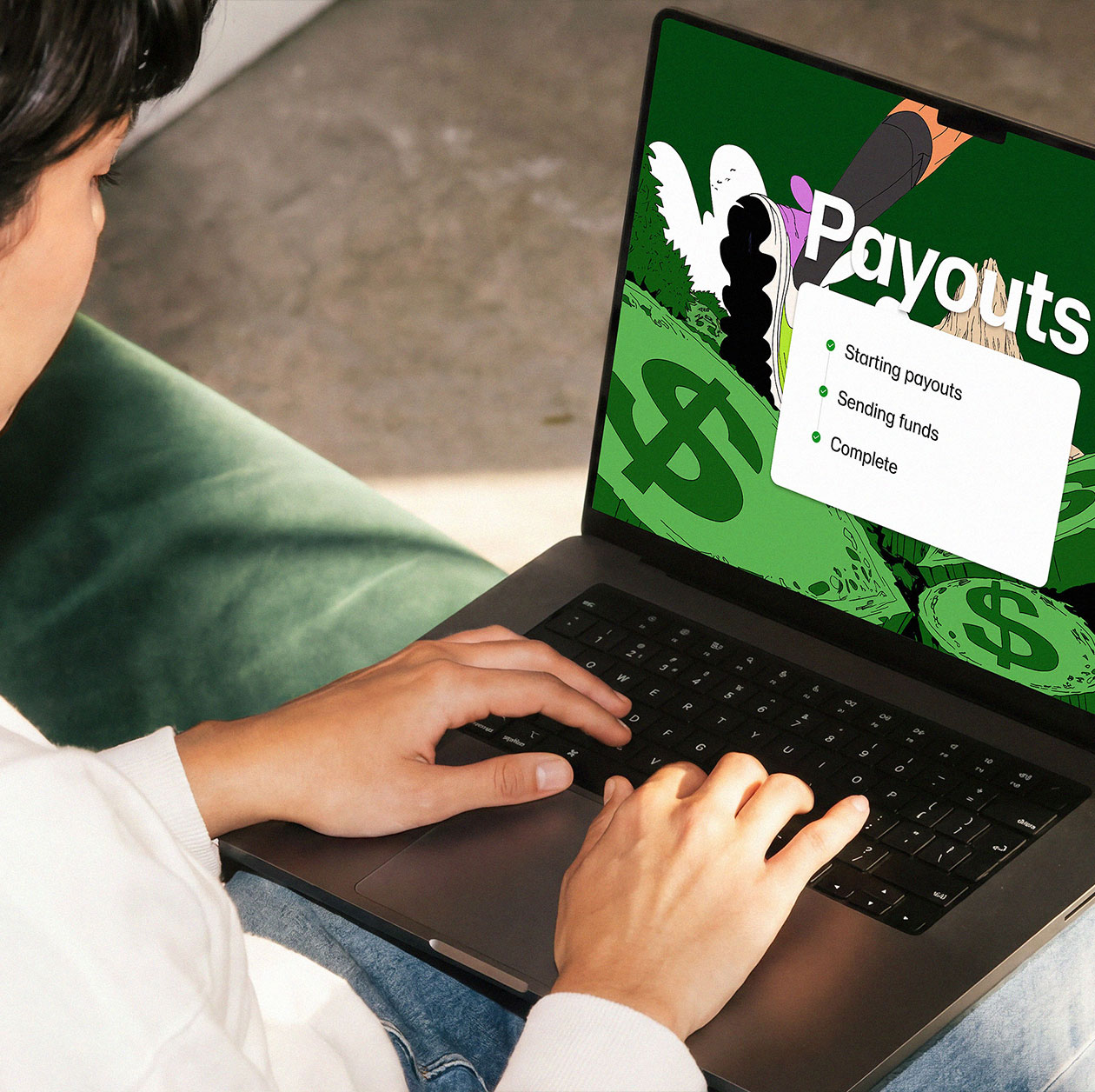 Person working on a laptop with a payouts dashboard open, seated in a green chair.