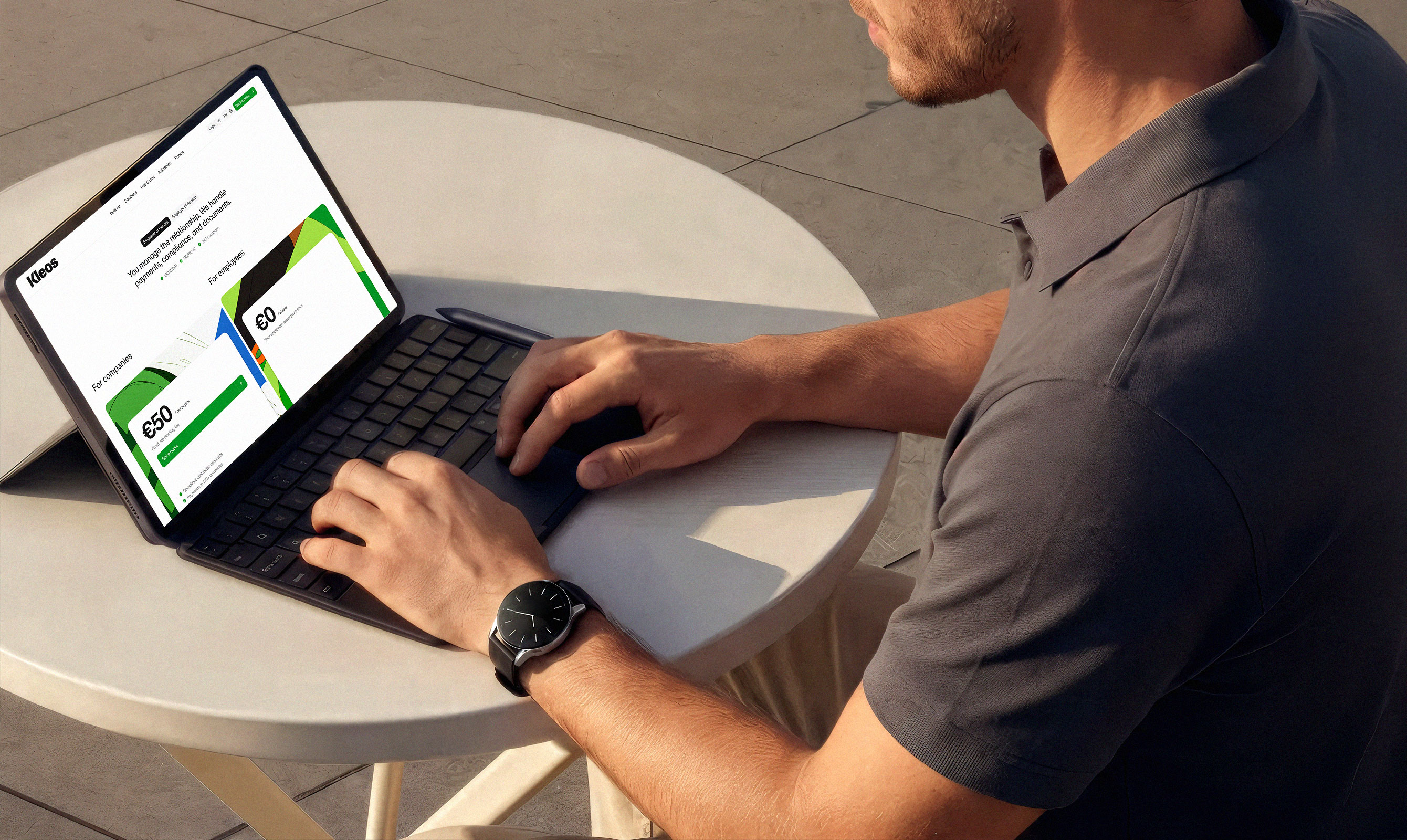 Man with a watch typing on a tablet displaying the Kleos pricing page outdoors
