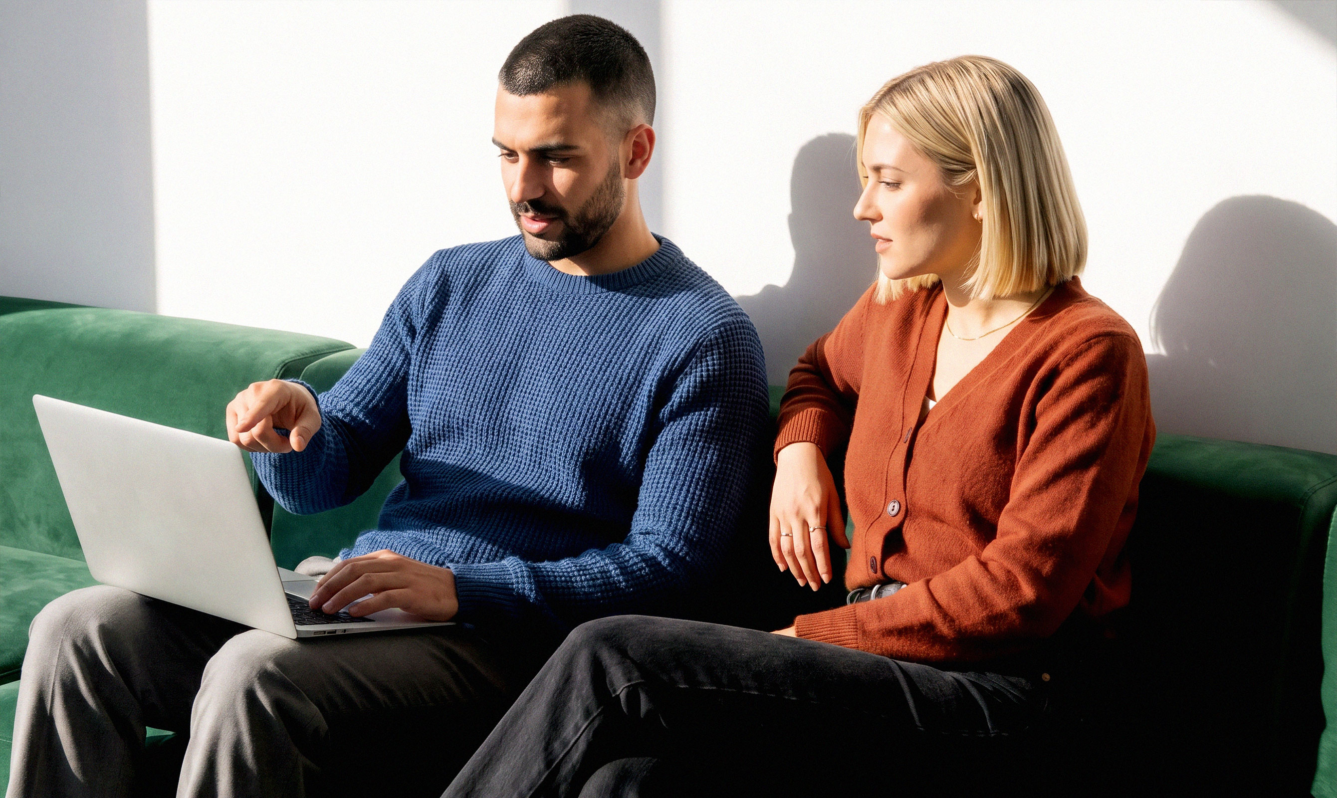 Two colleagues sitting on a green sofa reviewing work together on a laptop