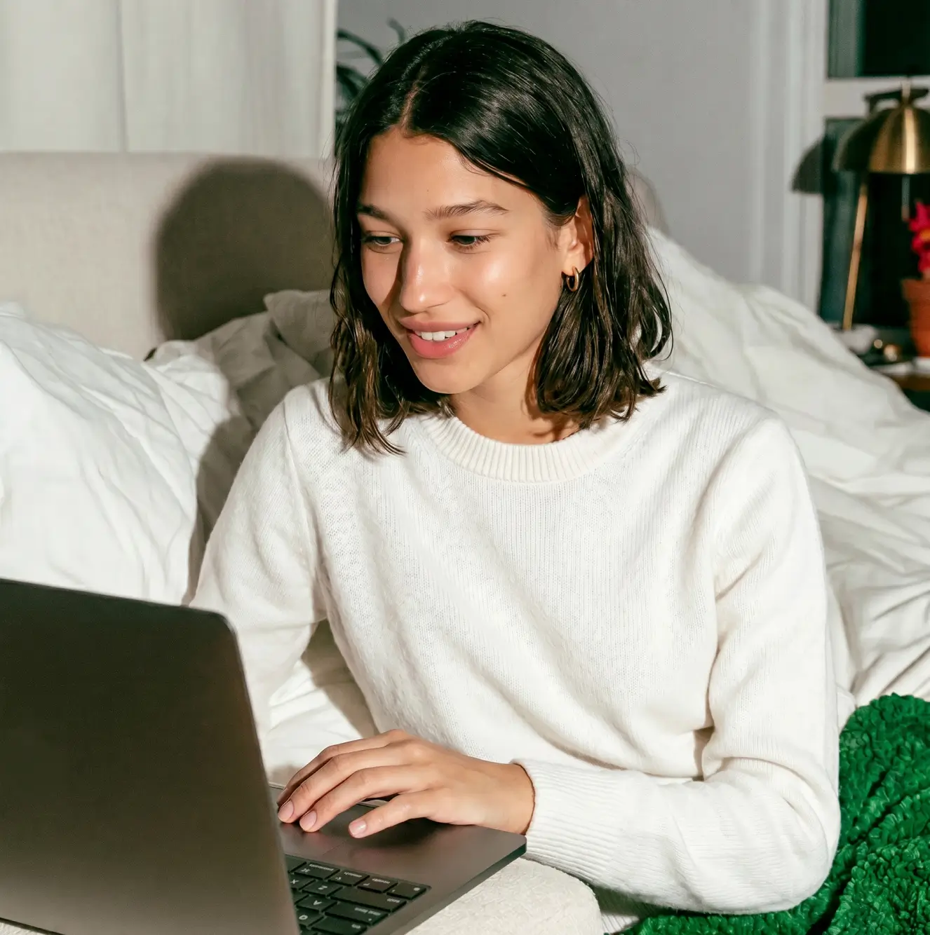 Smiling young woman in a white sweater working on her laptop at home