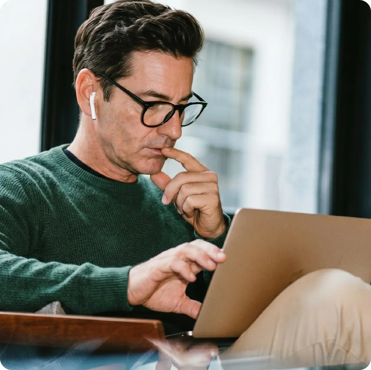 Focused middle-aged man with glasses and earbuds working on a laptop