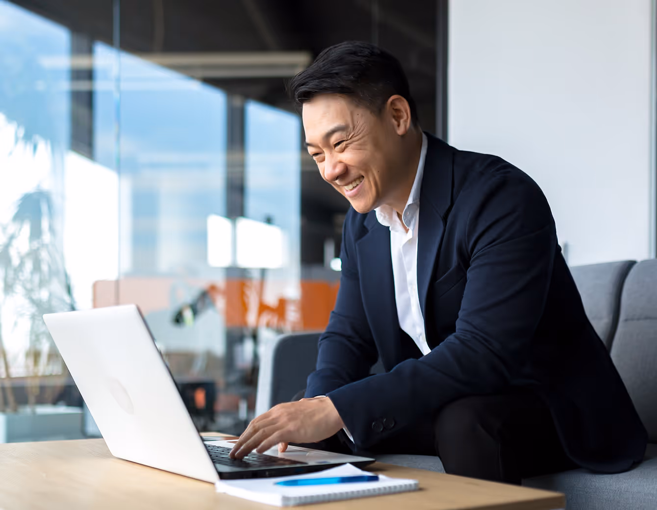 Smiling man in business attire working on a laptop in a modern office setting.