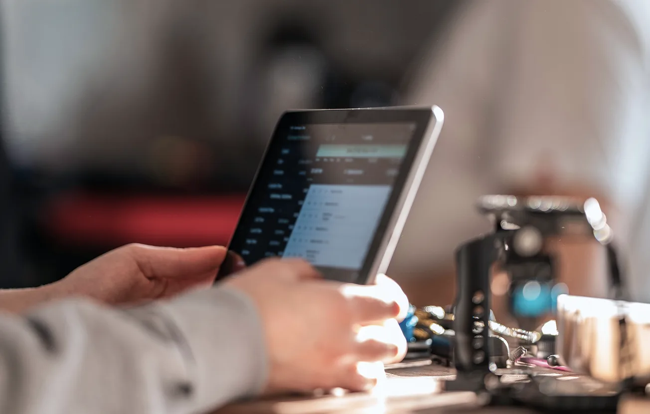 Person holding a tablet displaying a blurred screen with text on a table.