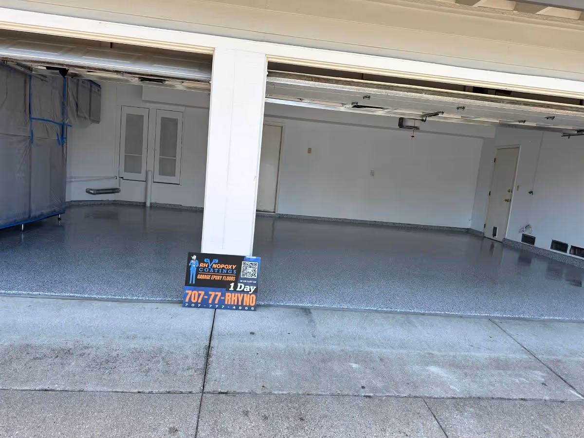 Wide residential garage with both doors open and a light gray flake floor, seen from the driveway