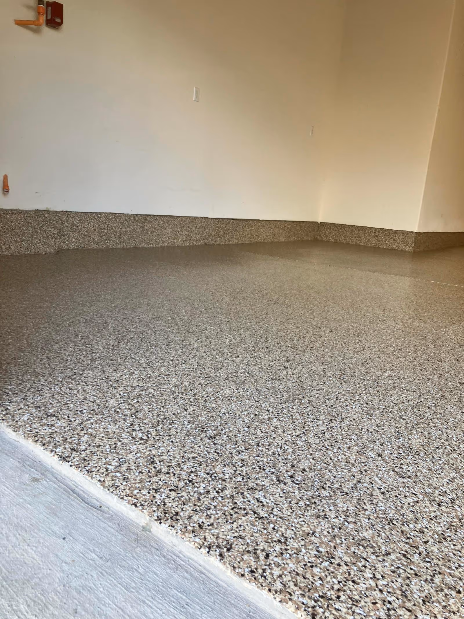 Tan flake garage floor with a coved flake wall base running around an empty corner