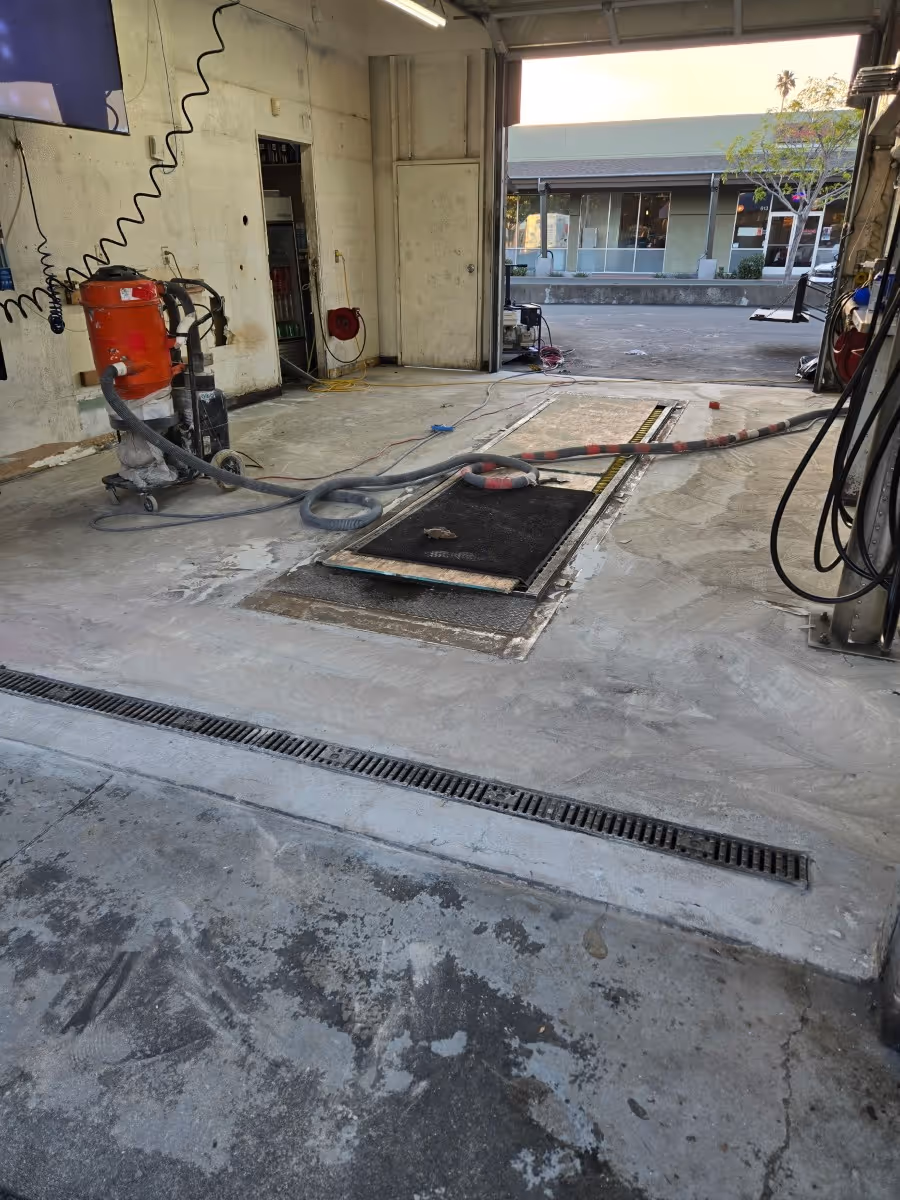 Concrete slab being prepared with a grinder and vacuum extractor beside a trench drain