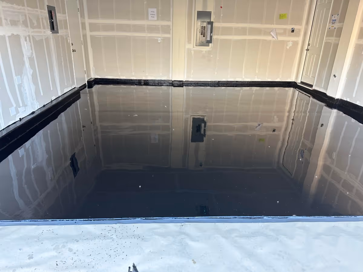 Dark gloss garage floor reflecting the empty garage walls, with a black coved base along the back