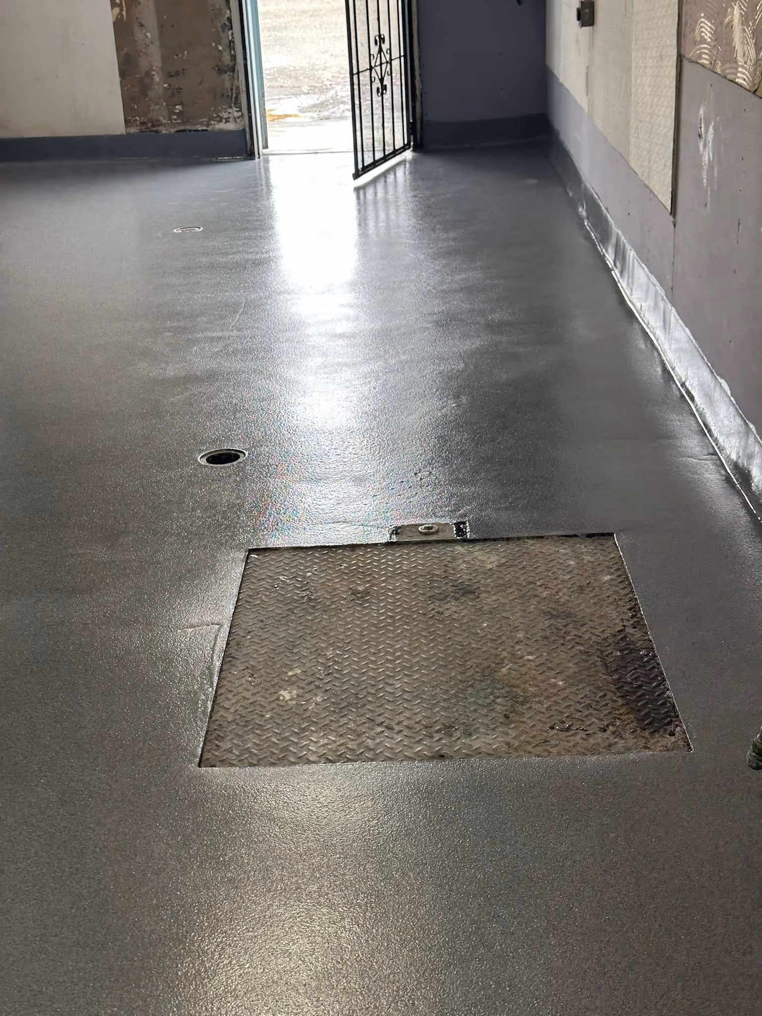 Gray commercial floor with a coved base, a floor drain and a steel access hatch set into it