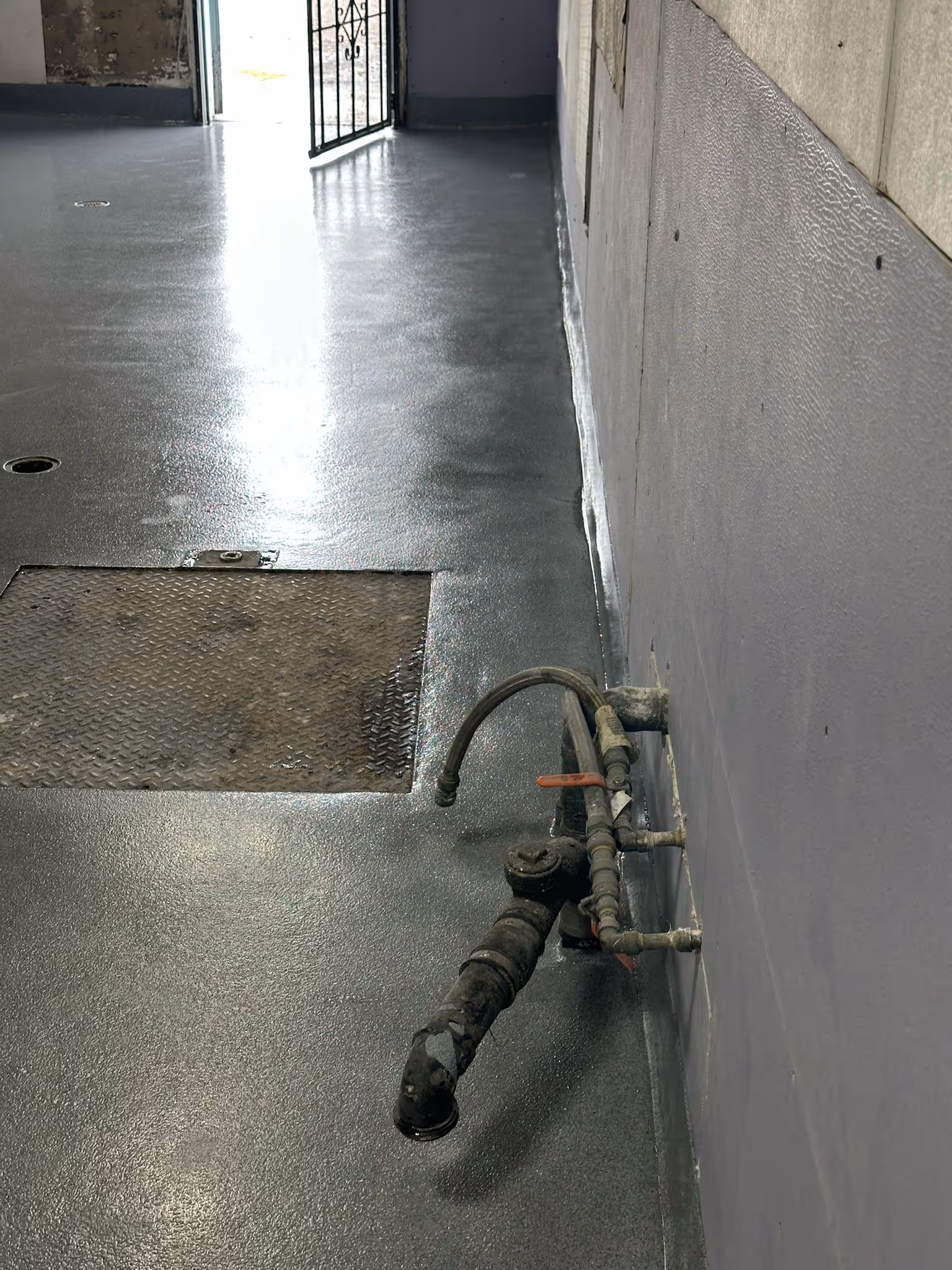 Coated industrial floor with a checker plate access hatch, floor drains and a coved wall base