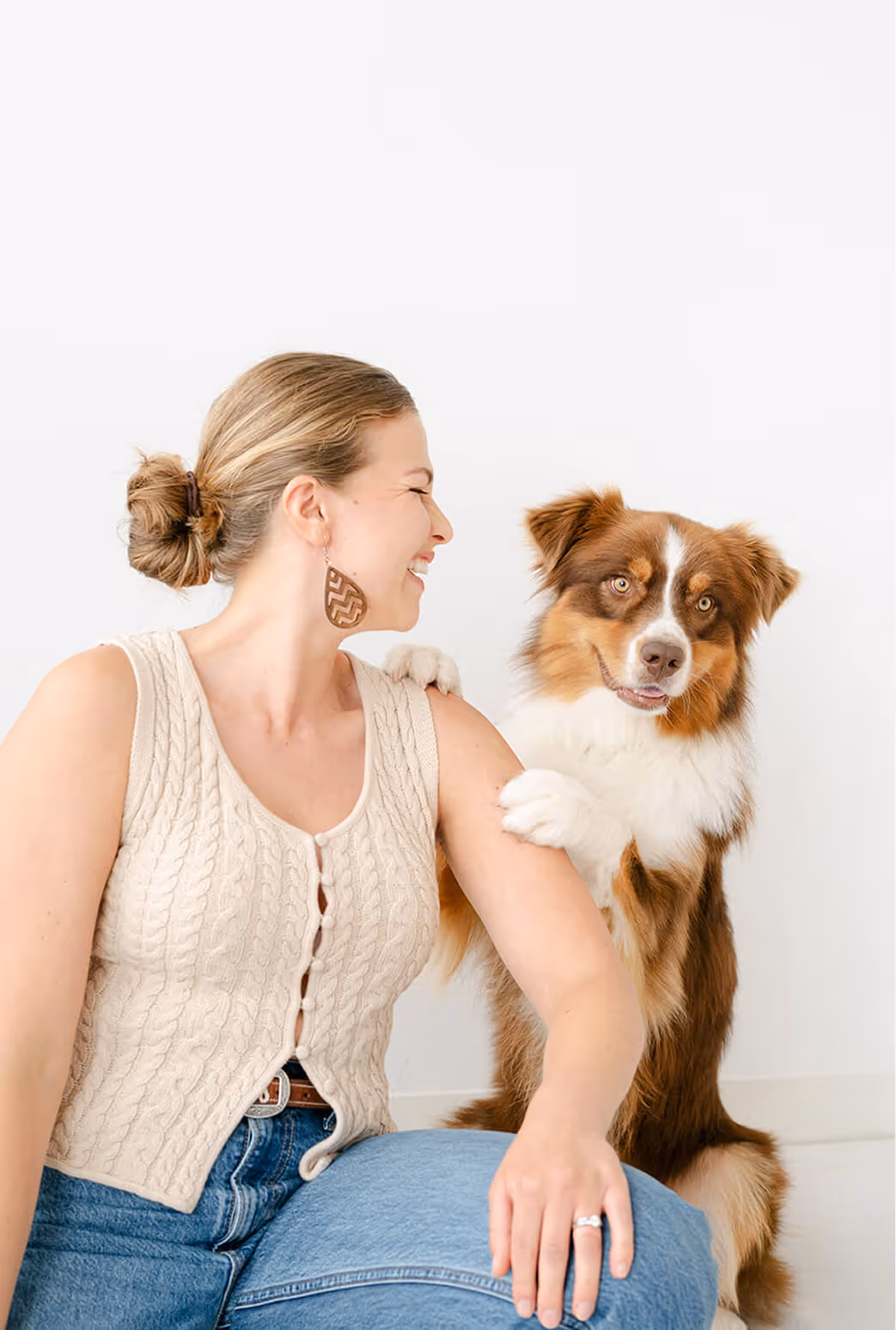 Smiling woman in a knitted top sits with a brown and white dog resting its paw on her shoulder.