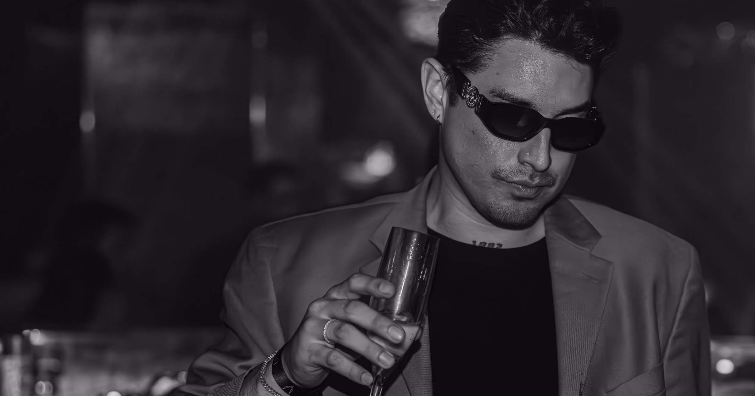 Guest in tailored evening attire holding a champagne flute inside Unveiled.