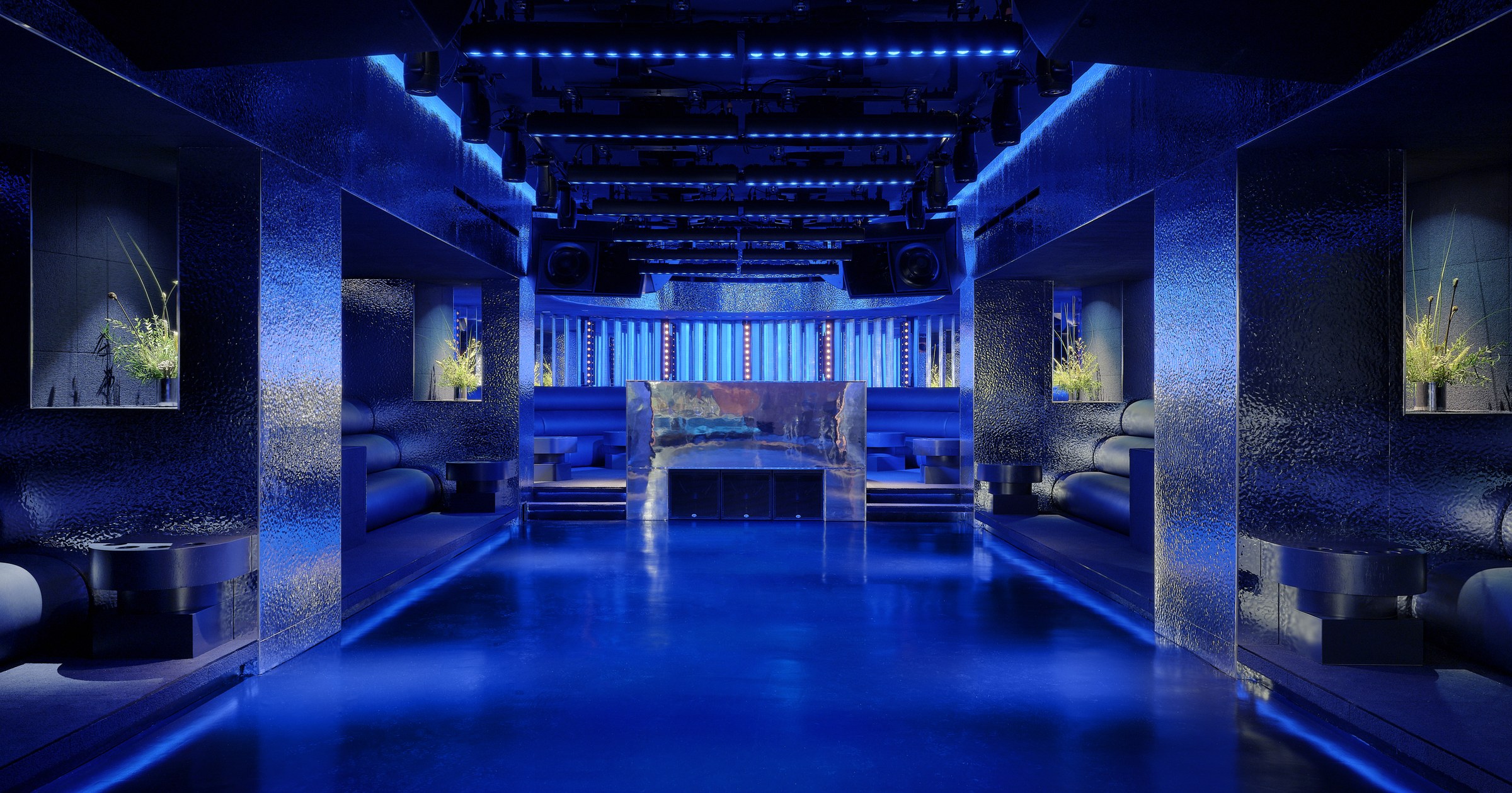 Wide blue-lit view of Unveiled showing the main floor, seating, stage, and circulation space.