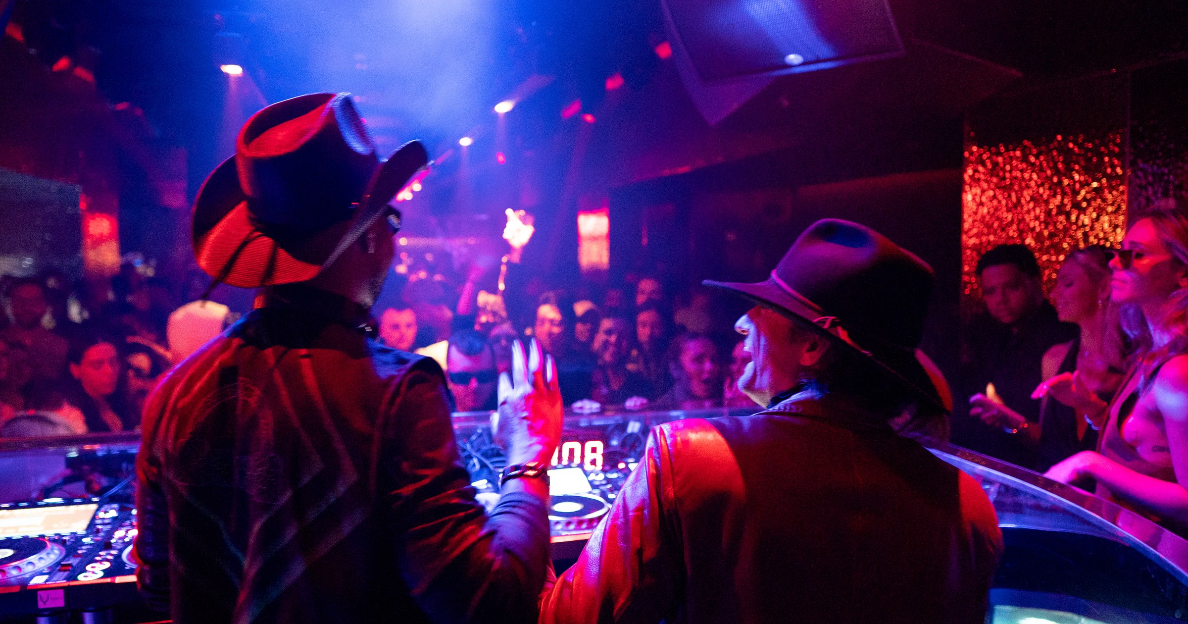 DJ performing at the Unveiled booth with a full crowd visible across the room.