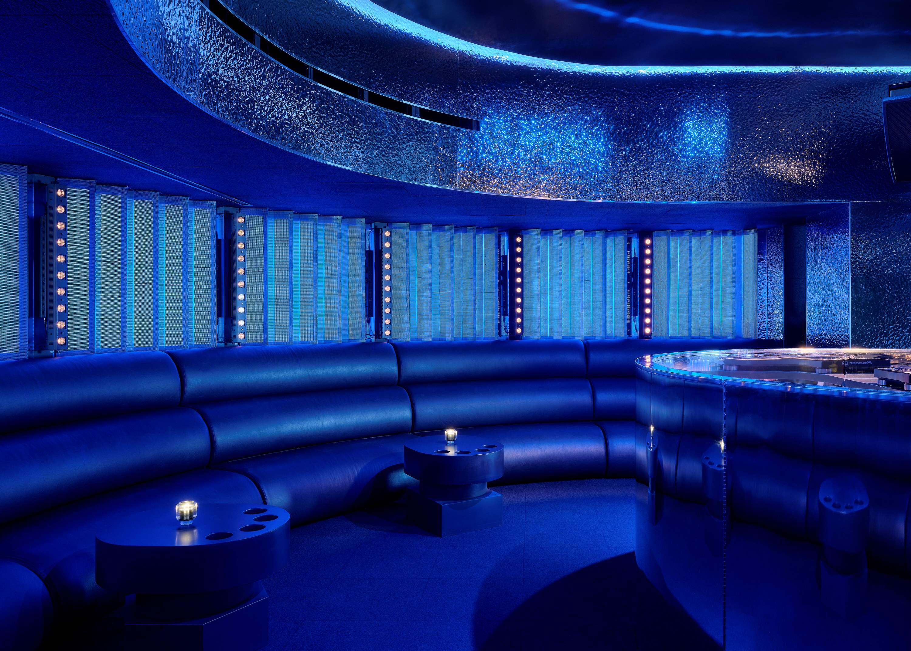 Wide blue-lit view of Unveiled showing the main floor, seating, stage, and circulation space.