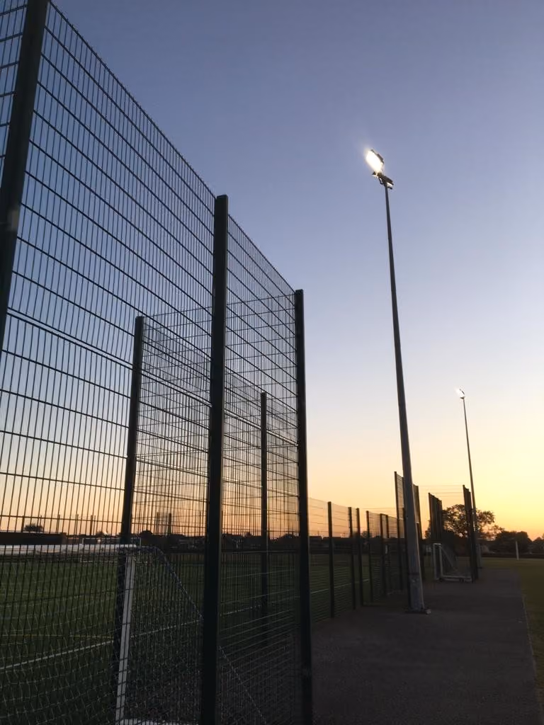 Floodlight tower and perimeter fencing at a sports pitch at dusk