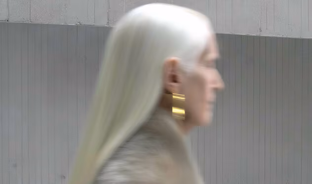 Side profile of a person with long white hair wearing large gold earrings and a fur garment.