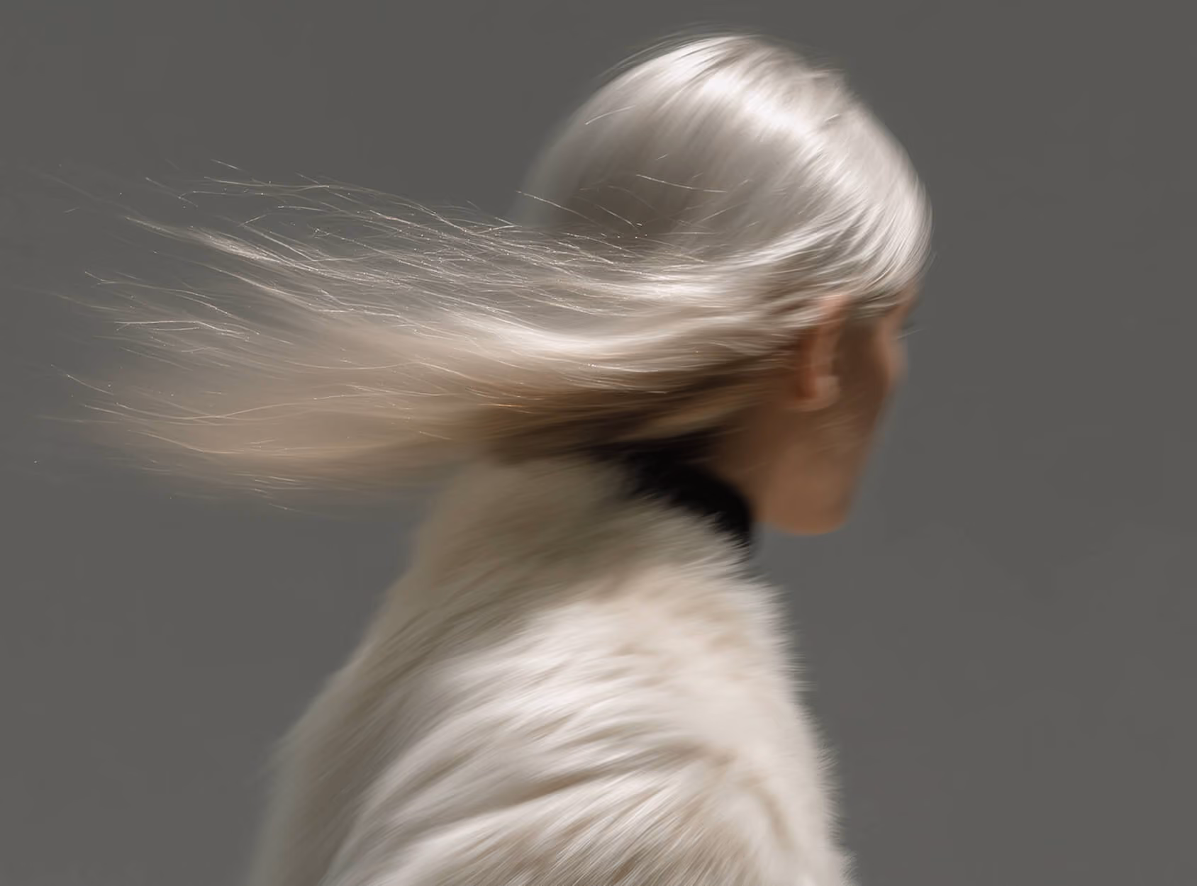 Person with long, pale blonde hair flowing to the left, wearing a white fuzzy sweater, facing right.
