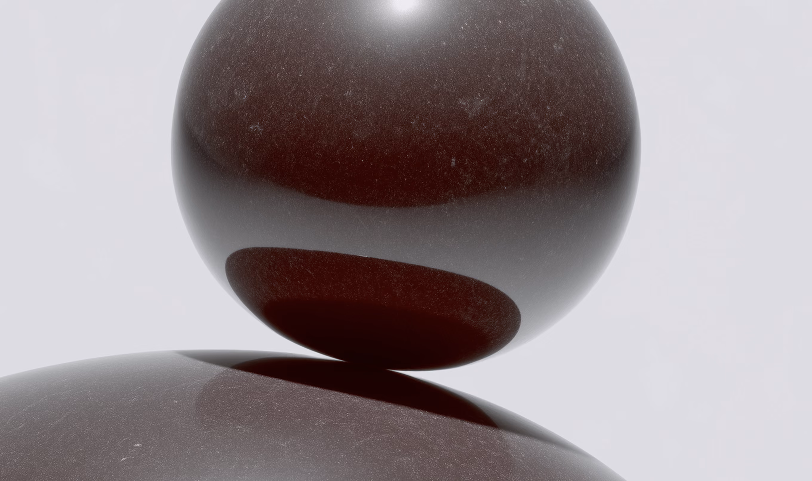 Close-up of two dark glossy spheres stacked on a light background.