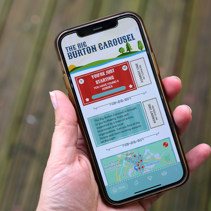 A hand holding a phone running the Big Burton Carousel trail app, built by Haywyre for Making Trails