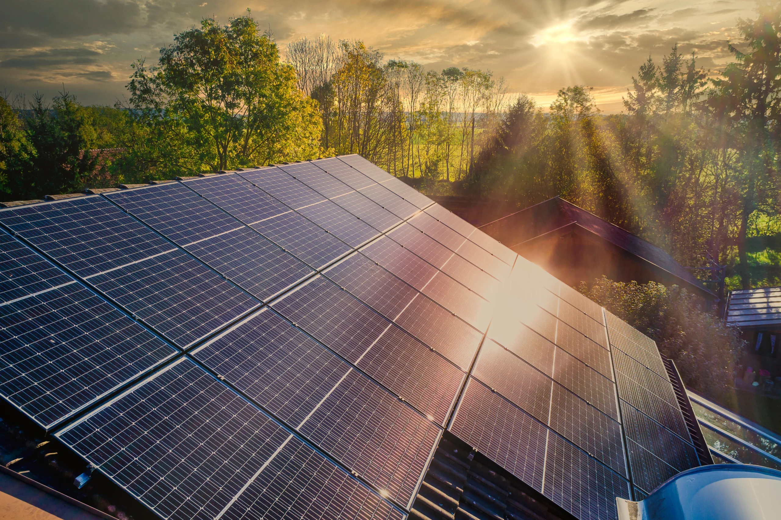 Solar panels installed on a rooftop reflecting sunlight with trees and a bright sky in the background.