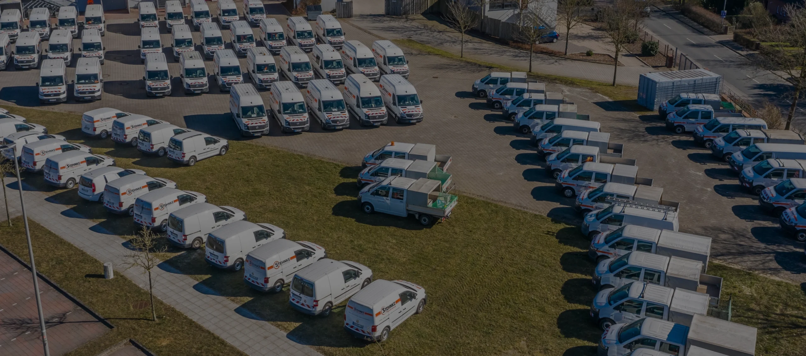 Luftaufnahme eines großen Parkplatzes mit zahlreichen weißen Transportern und kleinen LKWs, alle mit dem Logo „Stehnke“.