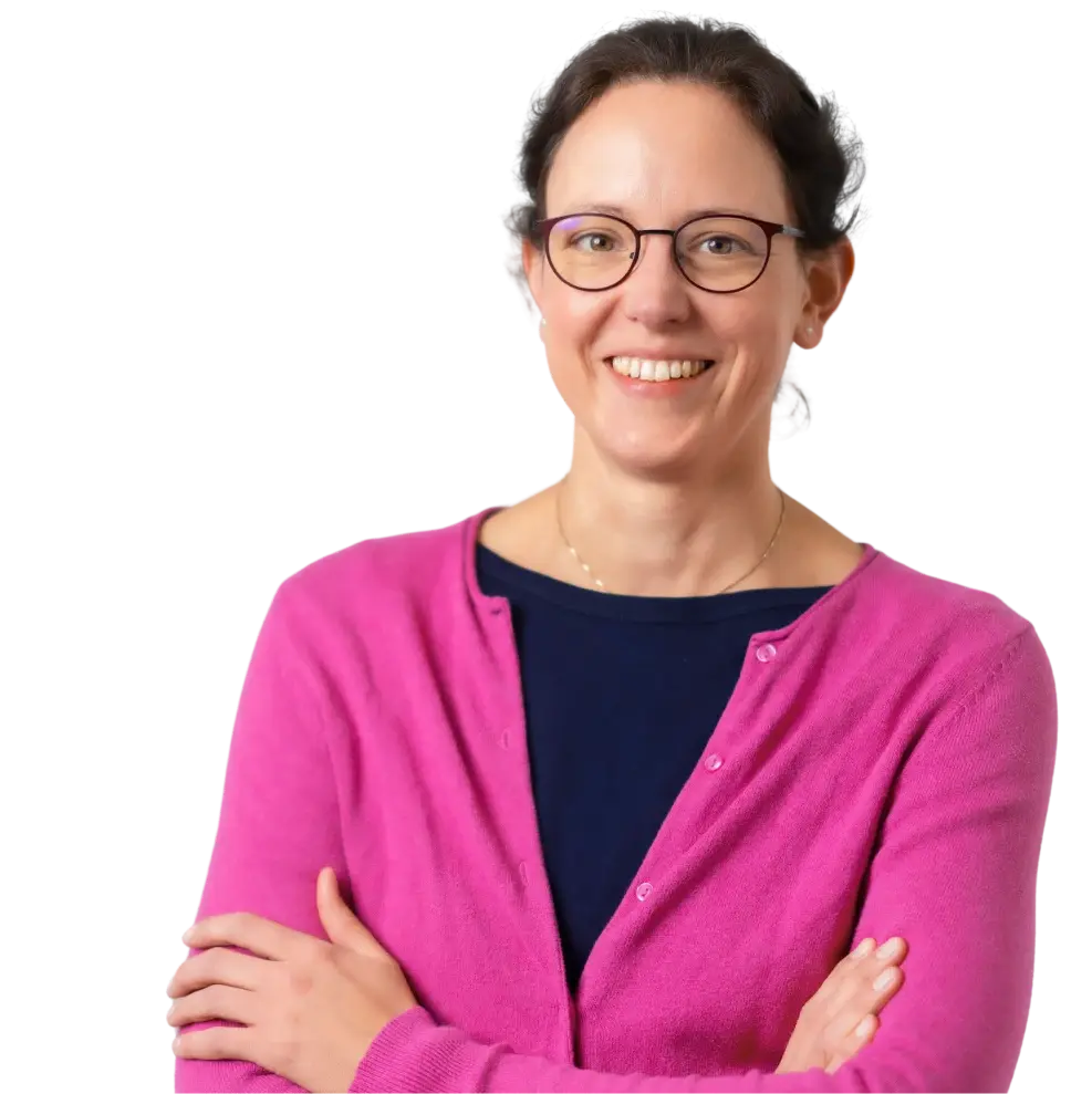 Lächelnde Frau mit Brille trägt rosa Strickjacke und navyblaues Shirt, Arme verschränkt.