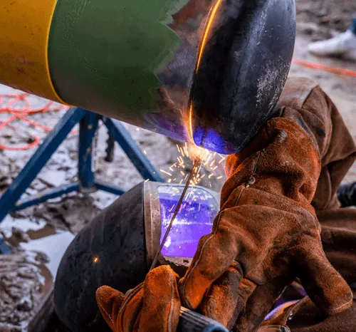 Person in protective gloves welding metal pipe with sparks flying.