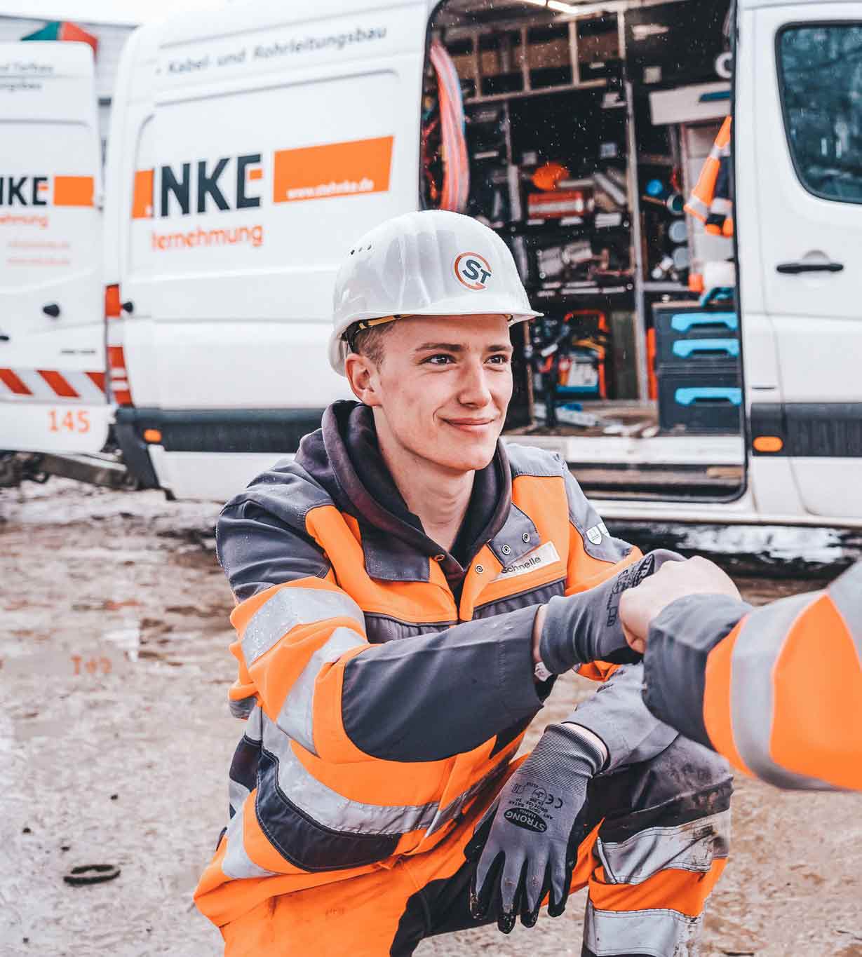 Bauarbeiter in orange- und grauer Schutzkleidung und Helm gibt eine Hände
