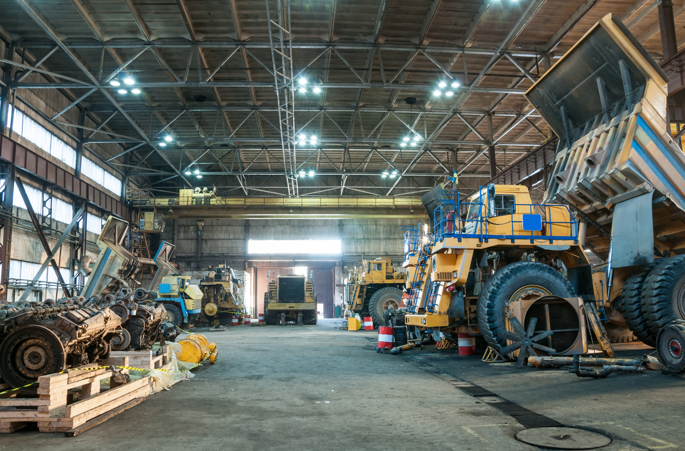 Interior of a large industrial garage with heavy mining trucks and machinery under maintenance.