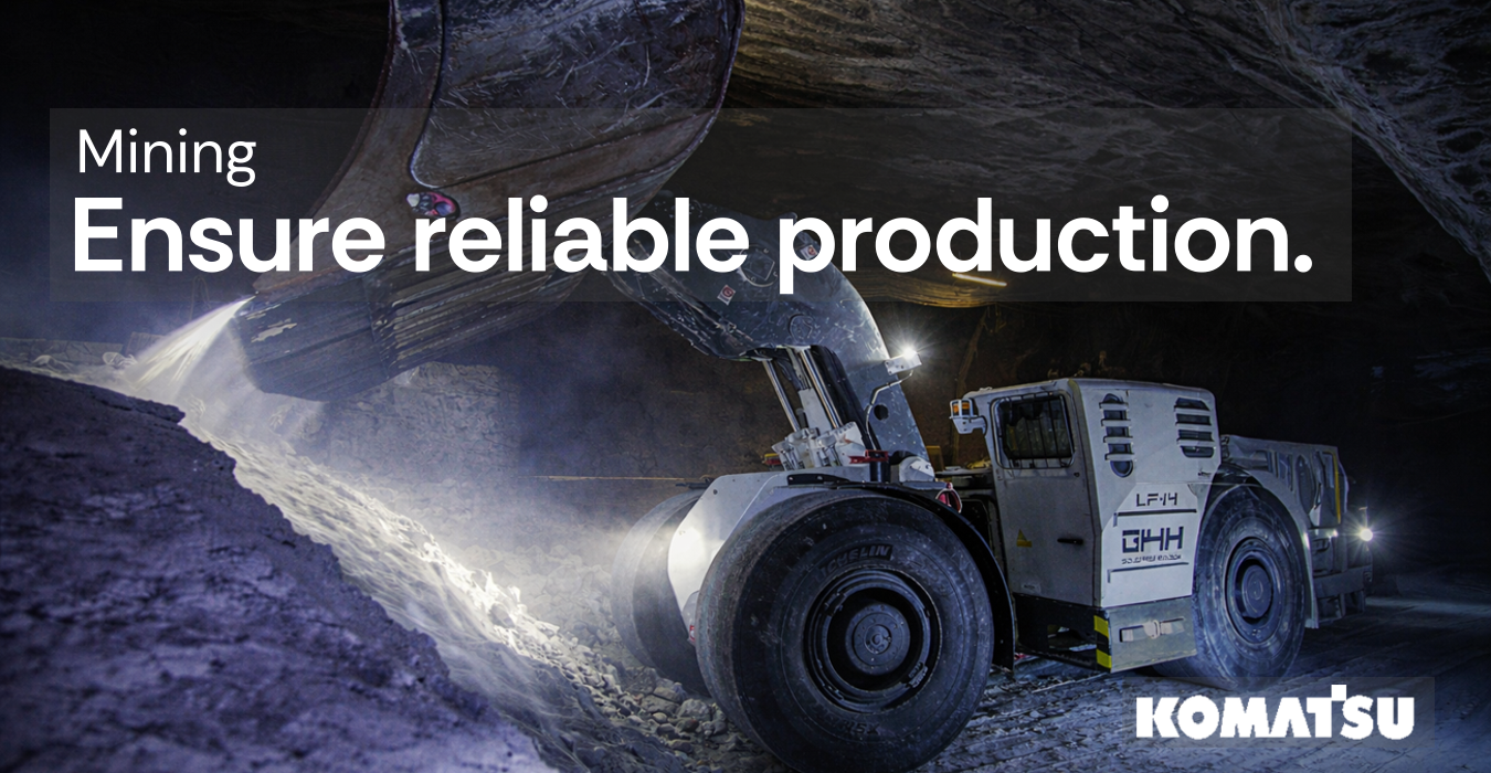 Underground mining loader vehicle scooping rocks inside a dimly lit mine tunnel.