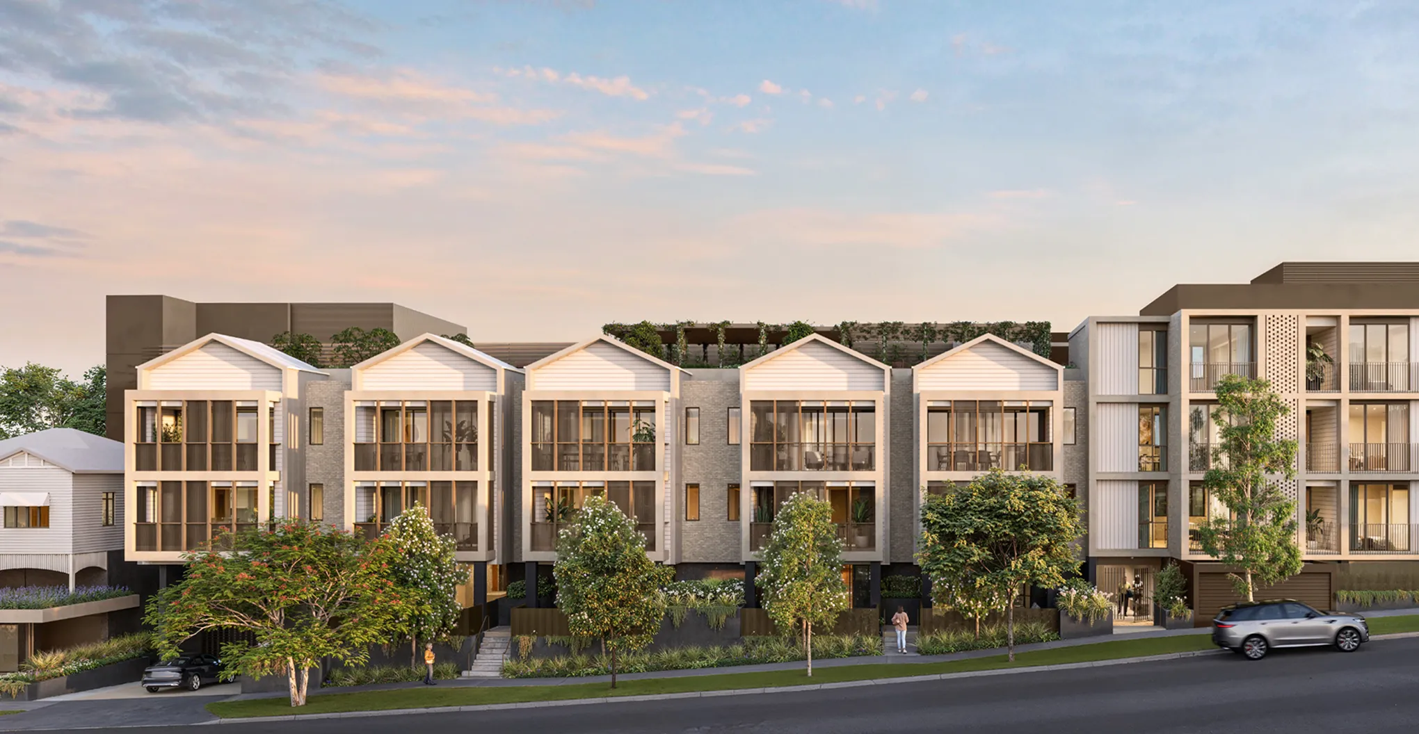 Modern residential complex of townhouses and apartments with trees and cars on the street at sunset.