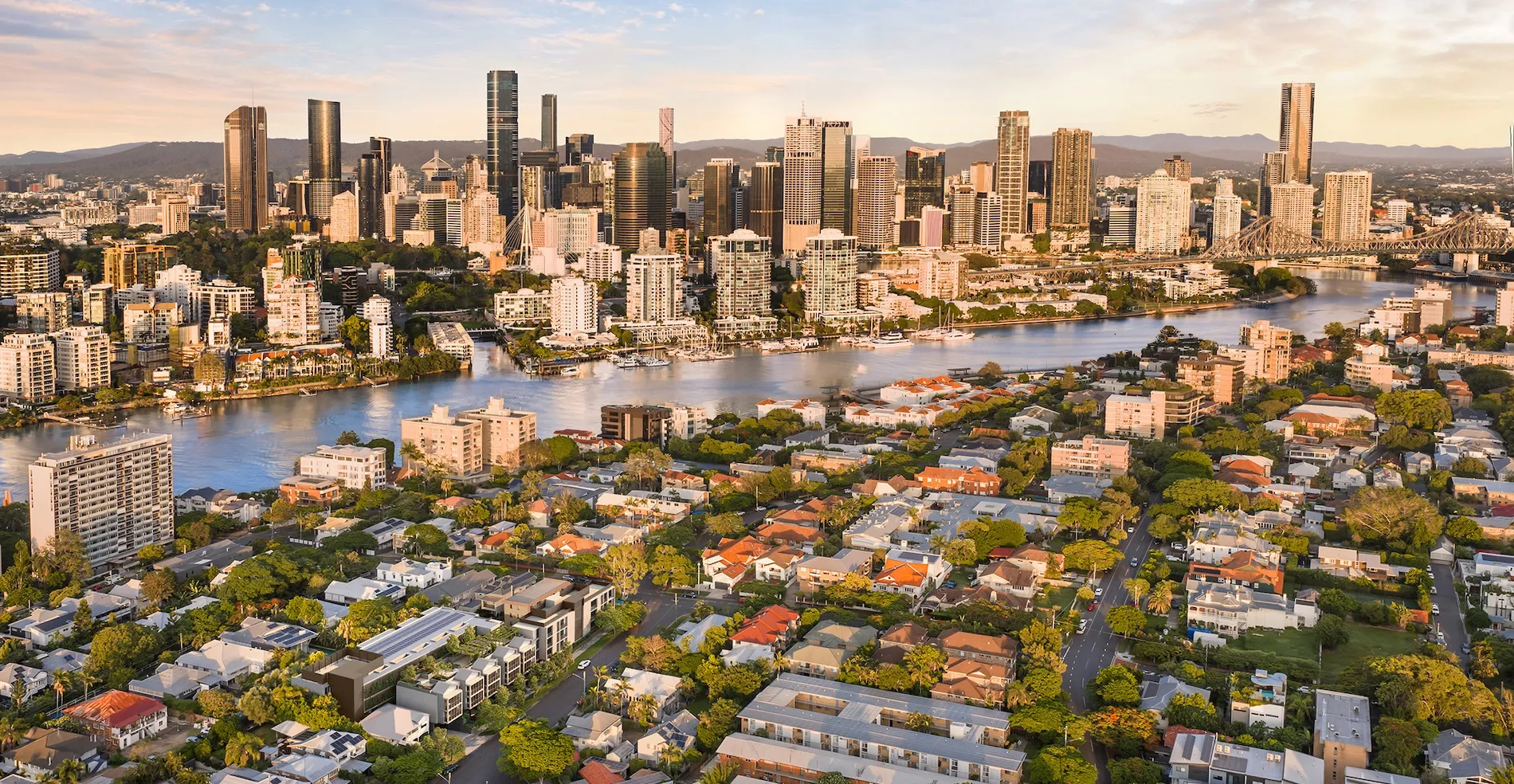 Aerial view of a city skyline at sunset with a river and residential areas in the foreground.