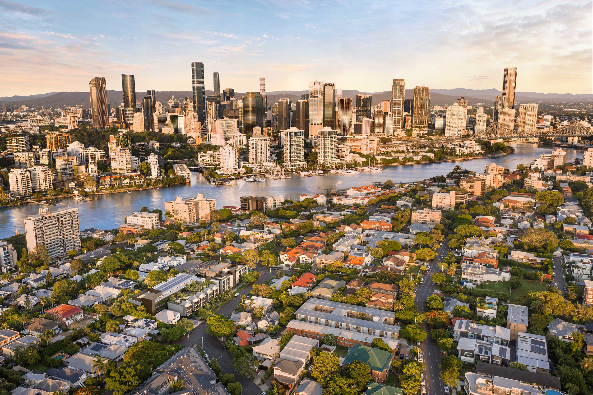 Aerial view of a city skyline at sunset with a river and residential areas in the foreground.