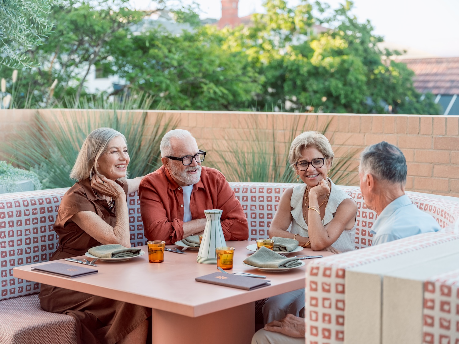 Four older adults seated outdoors around a table engaged in friendly conversation at a restaurant.