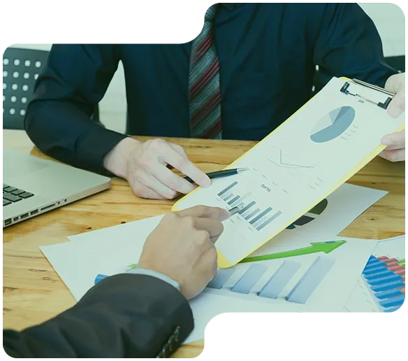 Två personer analyserar diagram och grafer på papper och en clipboard vid ett träbord.